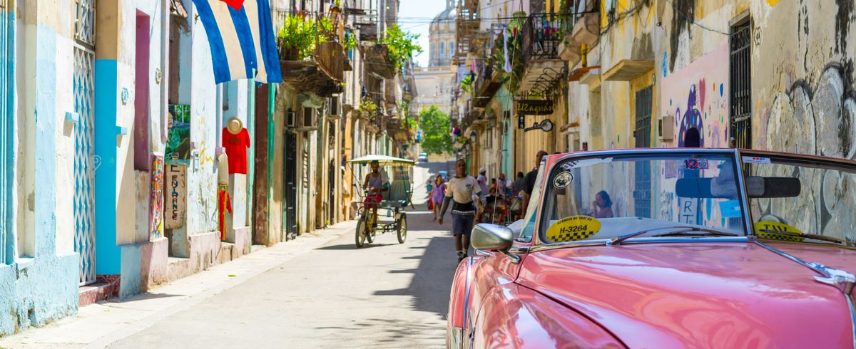 Photo of nameless street in Cuba with cuban flag in background and red convertible in the front of the image